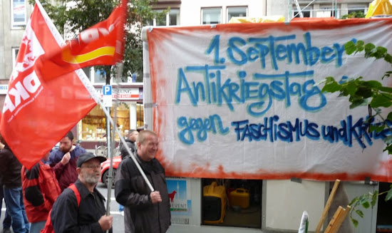 Demonstranten mit roten Fahnen, Plakat: »1. September Antikriegstag gegen Faschismus und Krieg«.