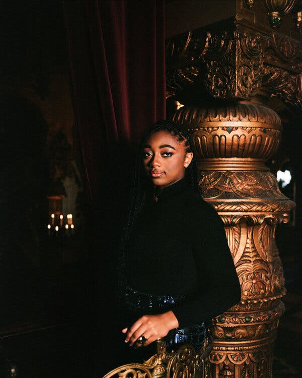 Joy, dressed in back, poses against a large brassy sculpture at a New York theater.