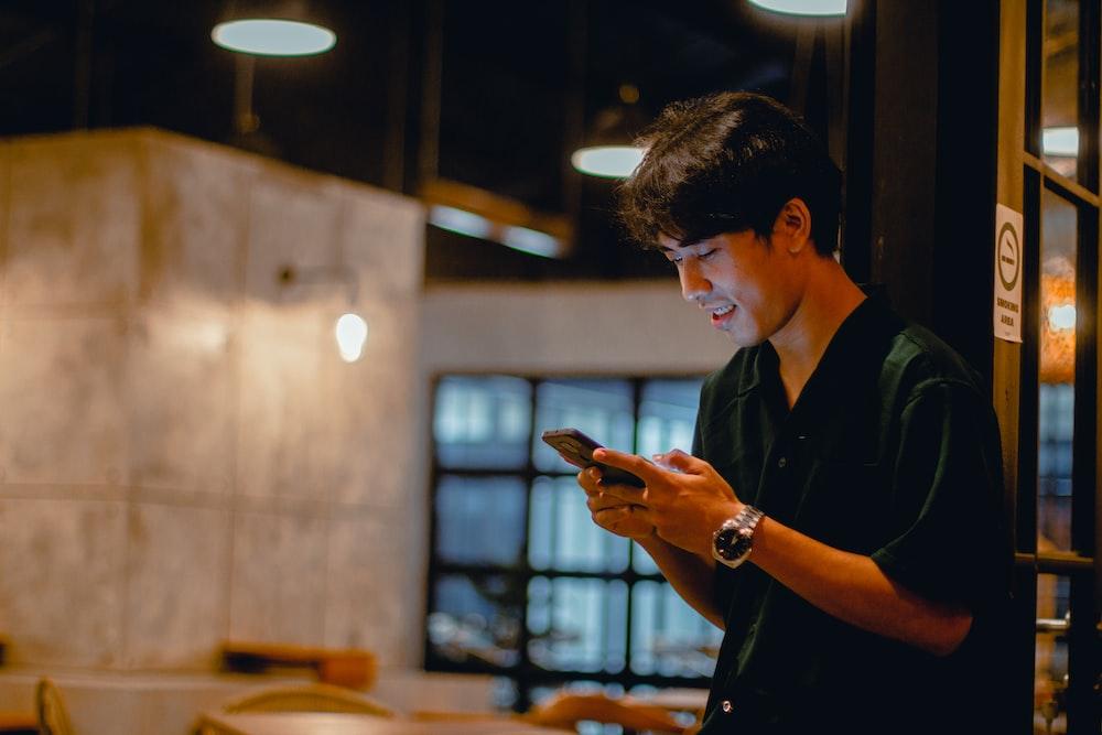 man in black polo shirt using smartphone