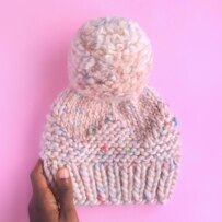 pink knit beanie with huge pom pom on pink background