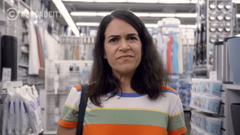 Abbi from Broad City standing in a Bed Bath and Beyond making a face like her stomach is aching.