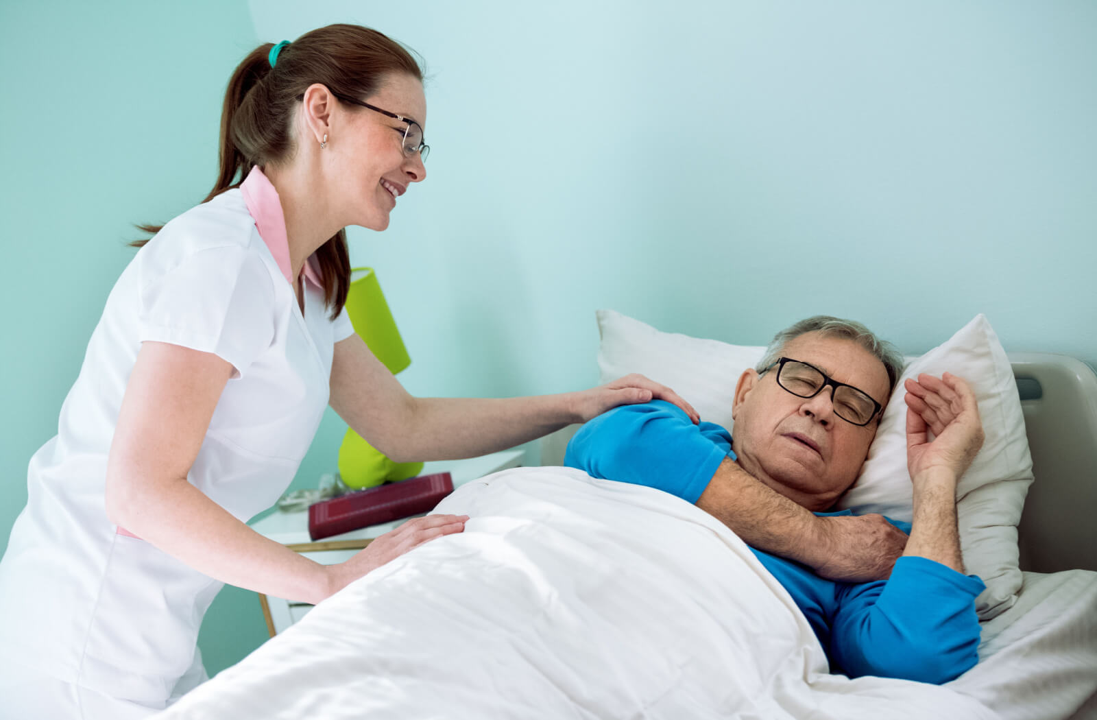 A female nurse helping an elderly man to sleep.