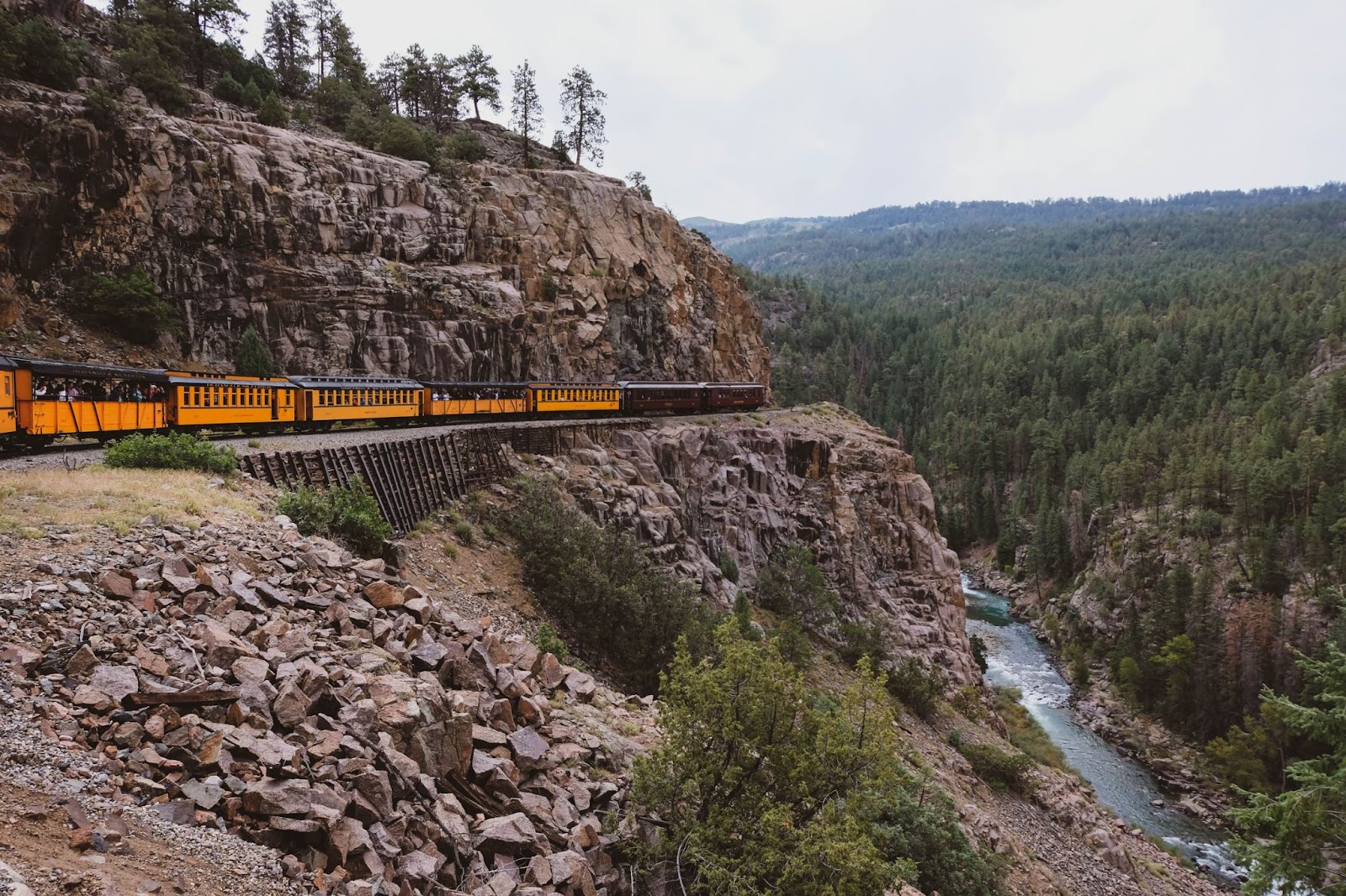 A landscape view of a train riding along the tracks with a river down below