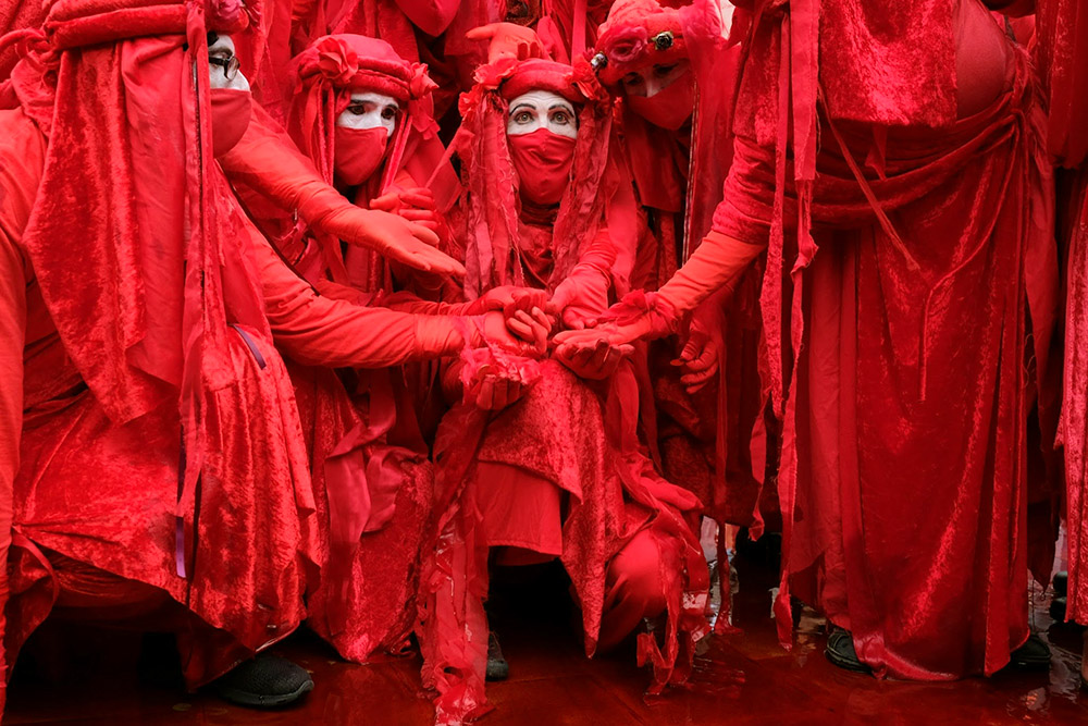 A group of red rebels crouch over a puddle of fake blood with mournful expressions.