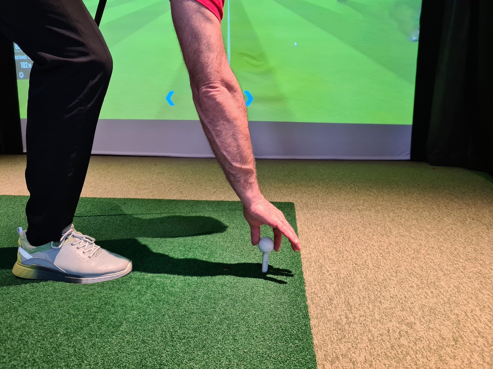 a golfer placing a golf ball on a tee in front of a golf simulator