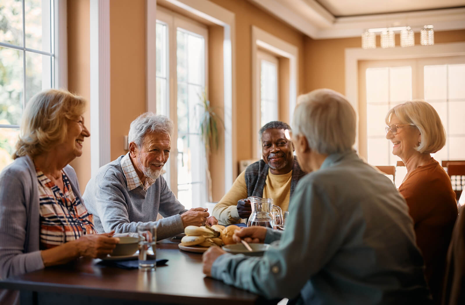 A group of seniors sitting around a table, eating and enjoying afternoon tea while smiling and chatting with each other.