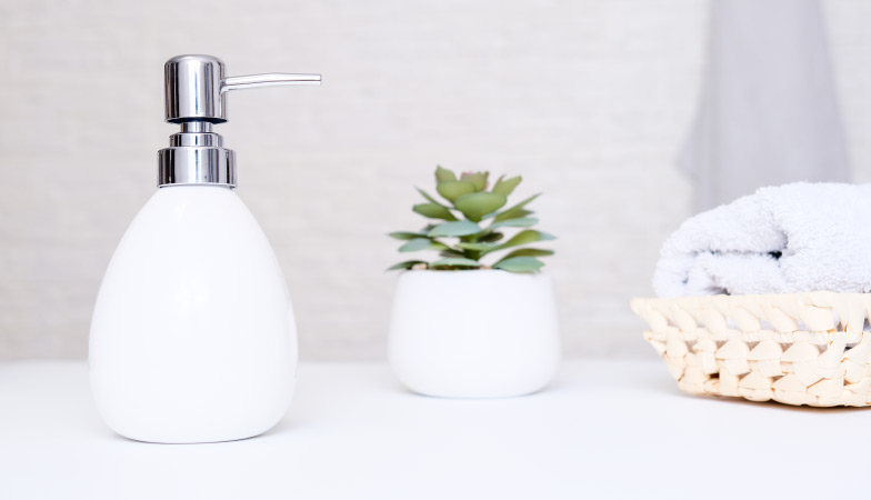 A hand soap dispenser beside a succulent plant and hand towel basket