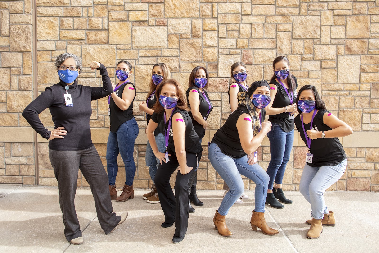 Group of people wearing masks showing their vaccination Band-Aid on their arms. 