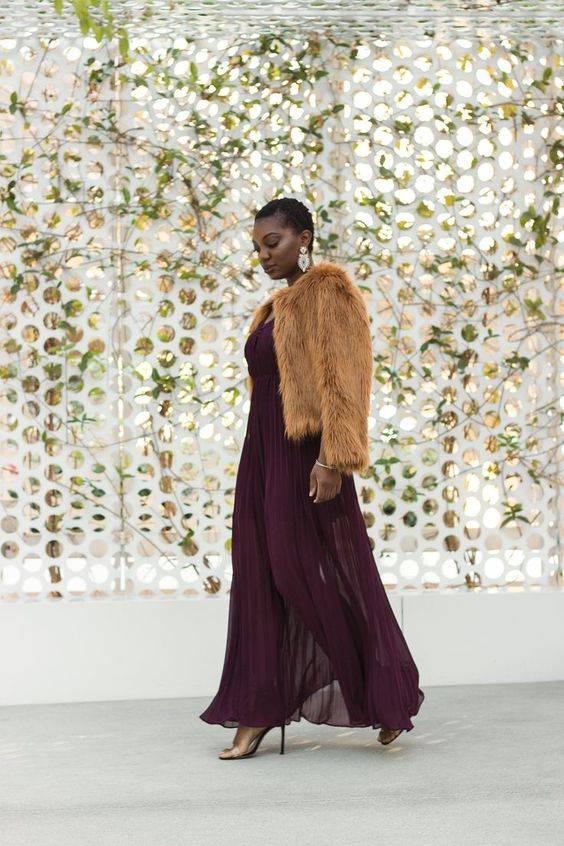 a lady in a burgundy maxi guest wedding dress for winter with a faux fur jacket