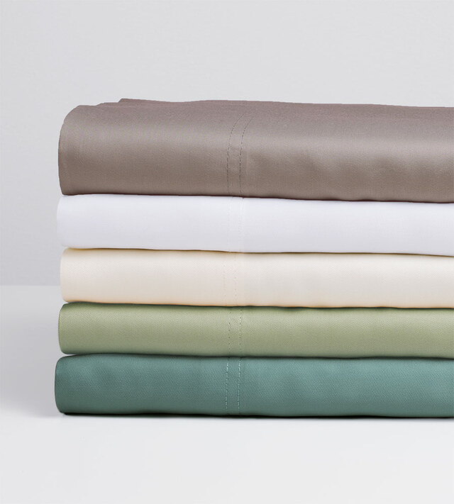 Neatly folded sheets in different colors stacked on a white surface.