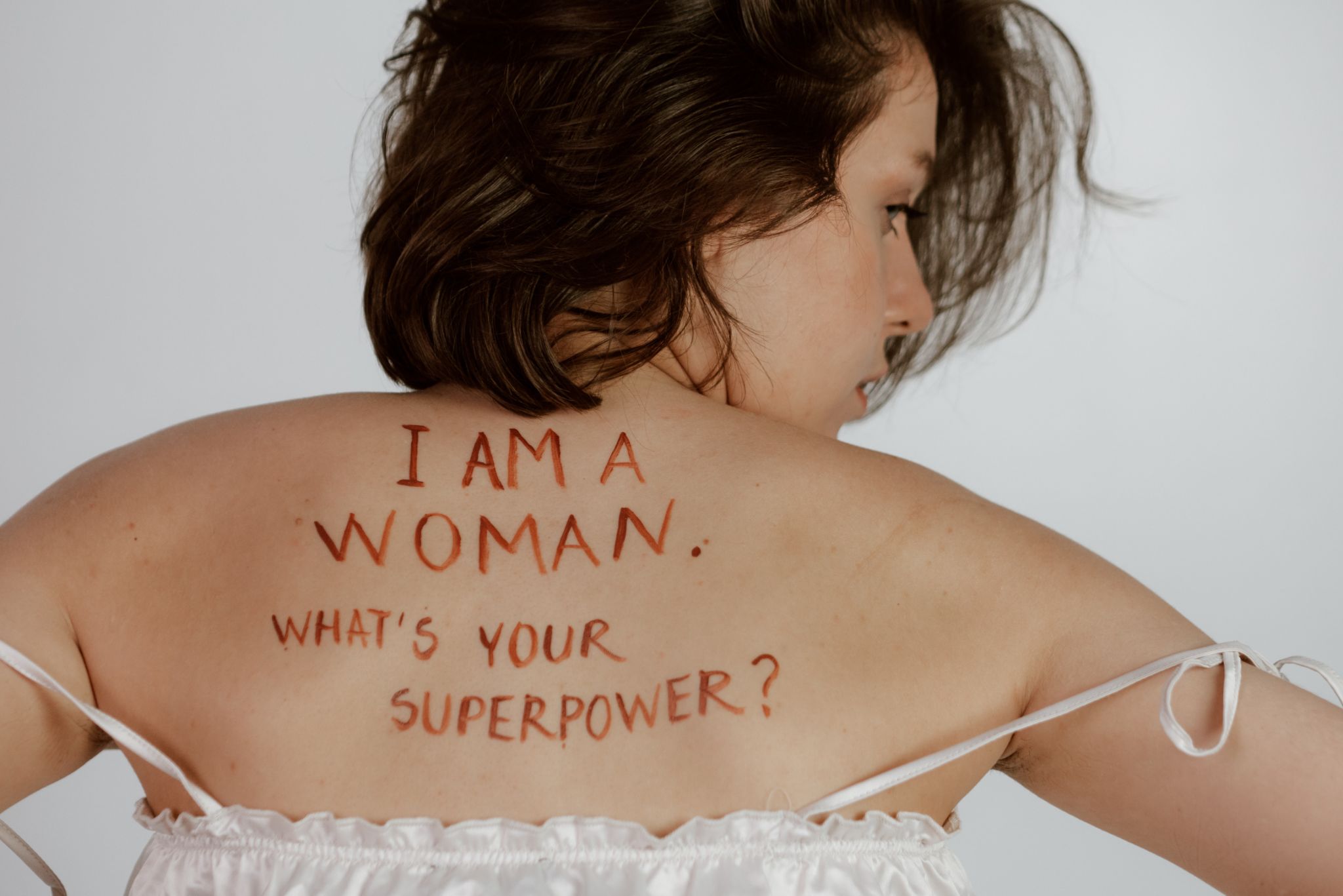 Mulher branca, com um escrito em suas costas: eu sou uma mulher, qual seu super poder?