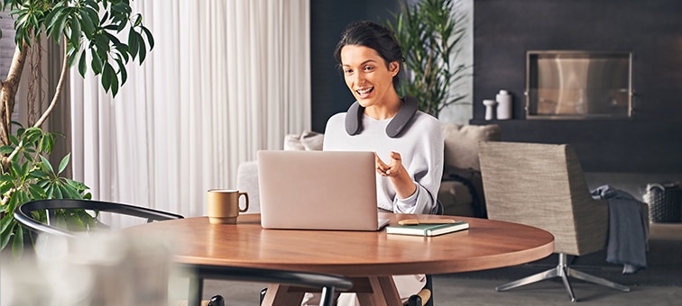 Woman sitting at a table with a laptop wearing SRS-NS7 during a hands-free call