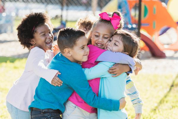 Group of multiethnic preschoolers hugging on the playground.
