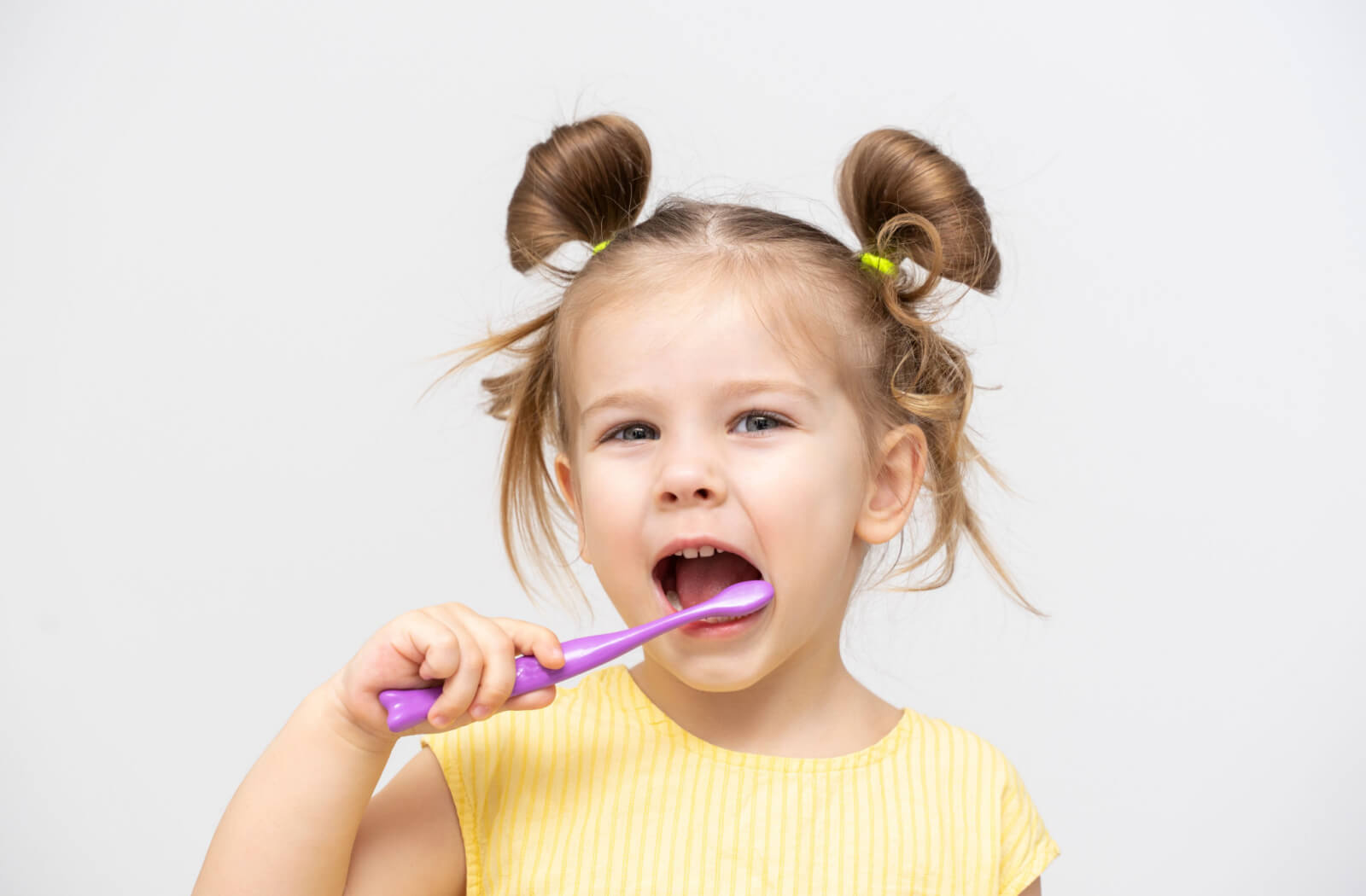 A young girl brushes her teeth with a purple toothbrush to prevent yellowing