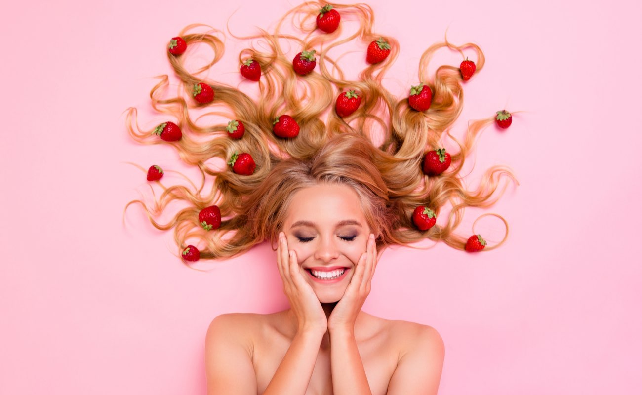 Woman smiling with strawberries in her hair on a pink background