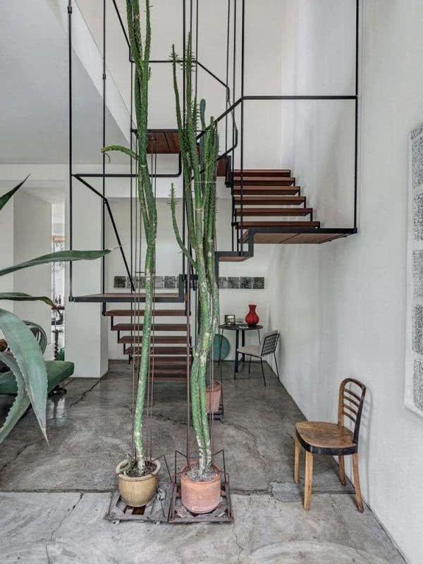 Escada com estruturas metálicas e degraus de madeira em ambiente com porcelanato rústico e vasos de plantas