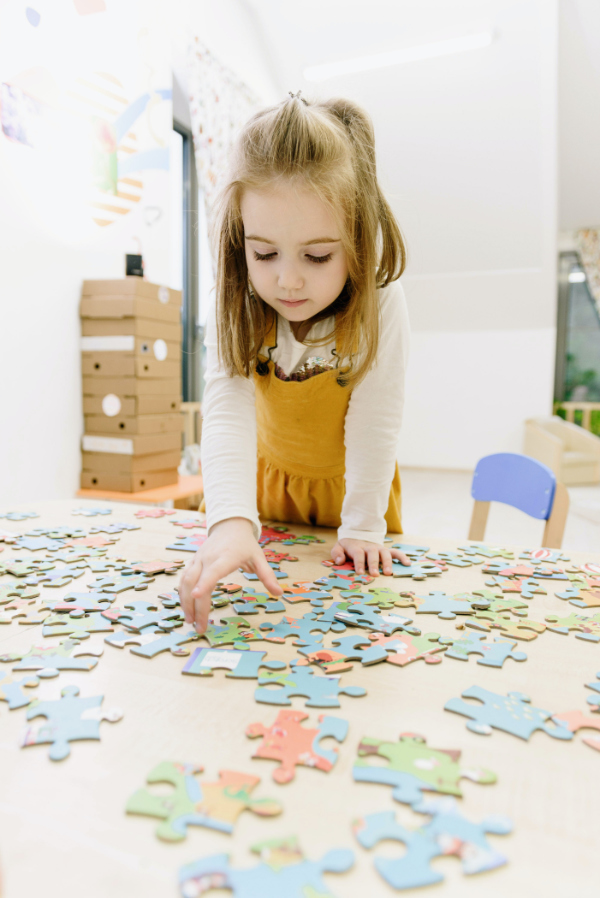 A young girl in a white and yellow dress standing at a table and working on a jigsaw puzzle.