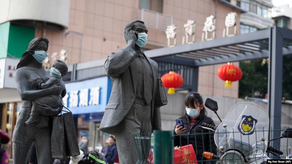 资料照片:在中国武汉市,一名女子正走过带着口罩的雕塑面前。世卫组织新冠溯源专家小组当时正在武汉考察。(2021年1月29日)