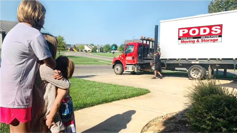 A woman and her children stand outside on a sunny day and watch a PODS driver preparing to transport their PODS portable moving container to their new home.