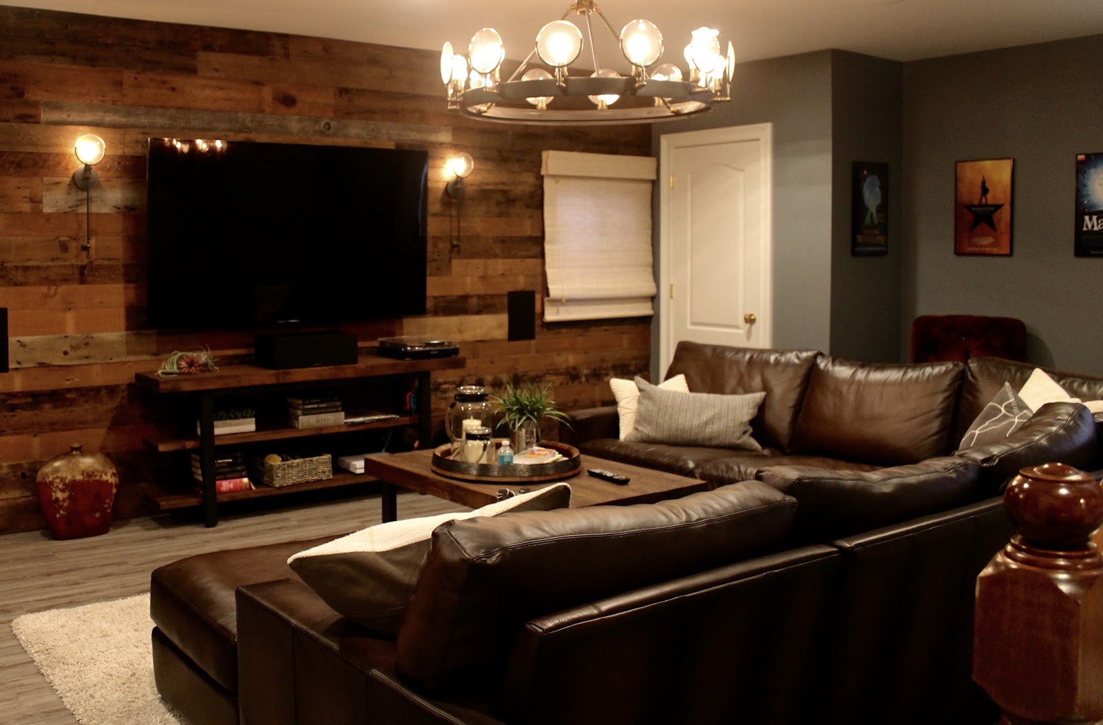 Basement media space with reclaimed wood walls, modern vintage chandelier, and leather couch.