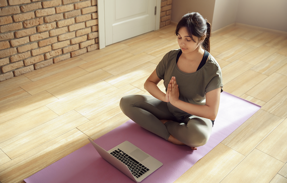 mental health technology: Woman meditating and doing yoga while watching on her laptop