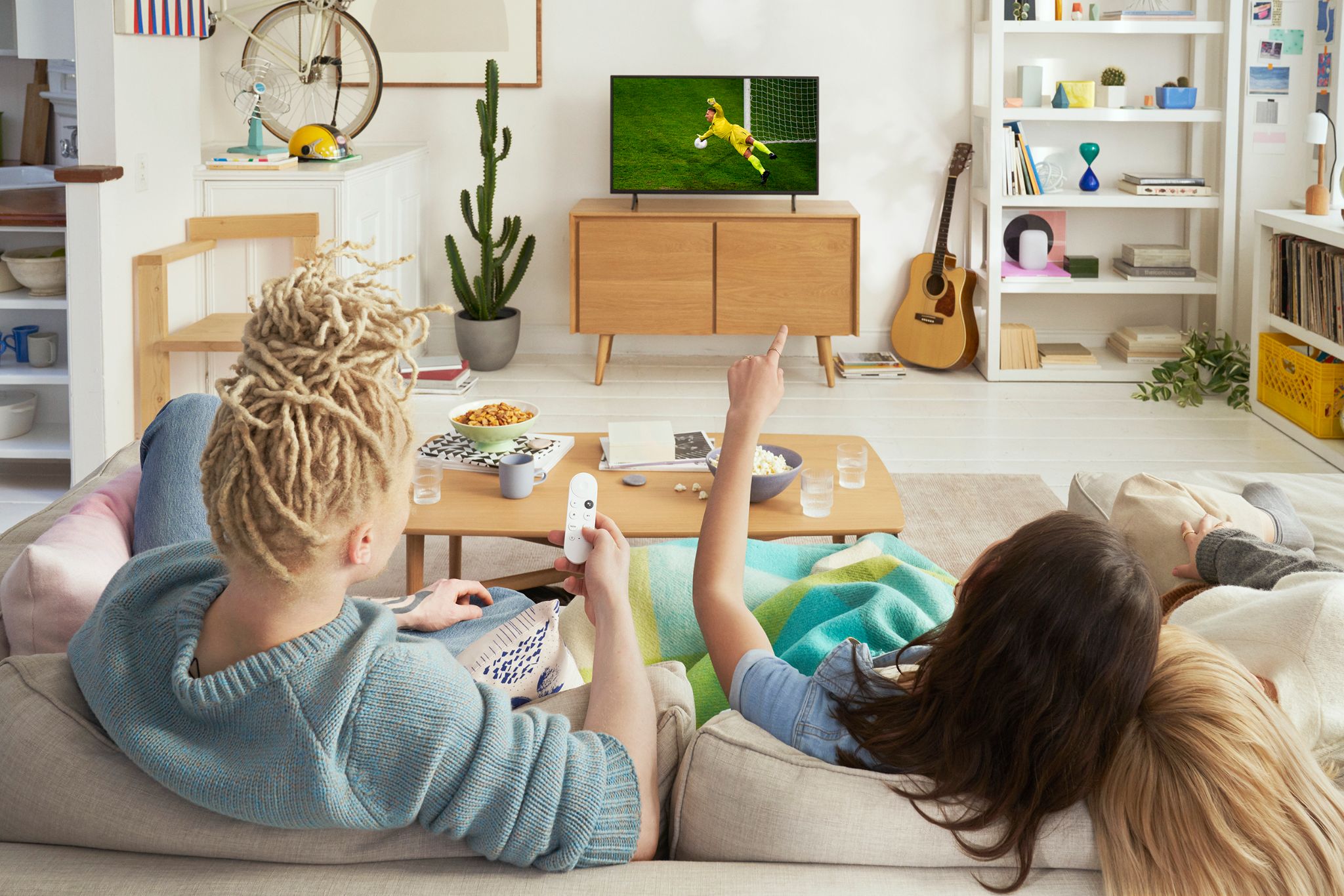 세 명의 친구가 거실 소파에 앉아 TV에서 Chromecast with Google TV (HD)로 축구 경기를 시청하고 있다.