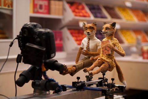 Behind the scenes of Fantastic Mr Fox. The stop motion models of Mr and Mrs Fox are sitting side by side, with a camera set up on a rig in front of them.