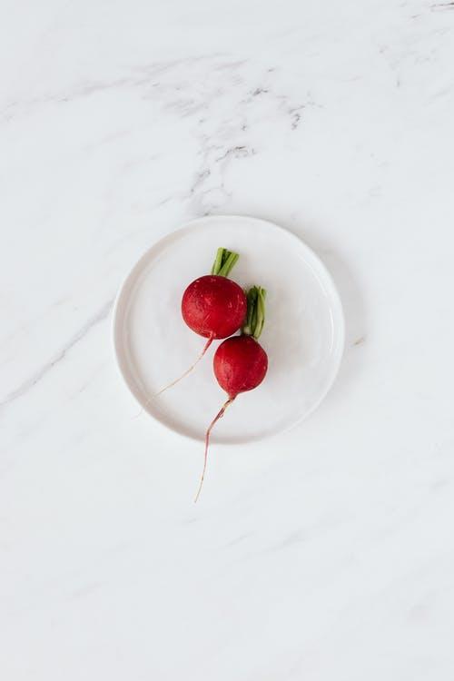 Top view of fresh red radishes placed in ceramic bowl standing on white marble table