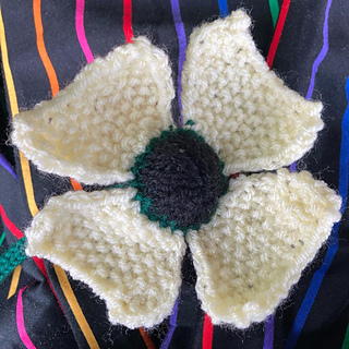 white knitted poppy with black center on colorful fabric background
