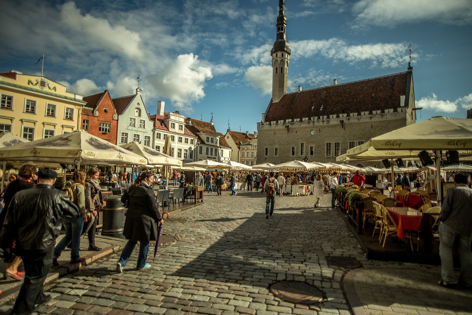 Tallinn old town, vibrant square full of outdoor restaurants and tourists wandering around. Large medieval cathedral in the background and traditional architecture.