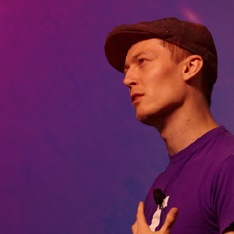 Photo of Orta therox in a purple shirt talking into a microphone.