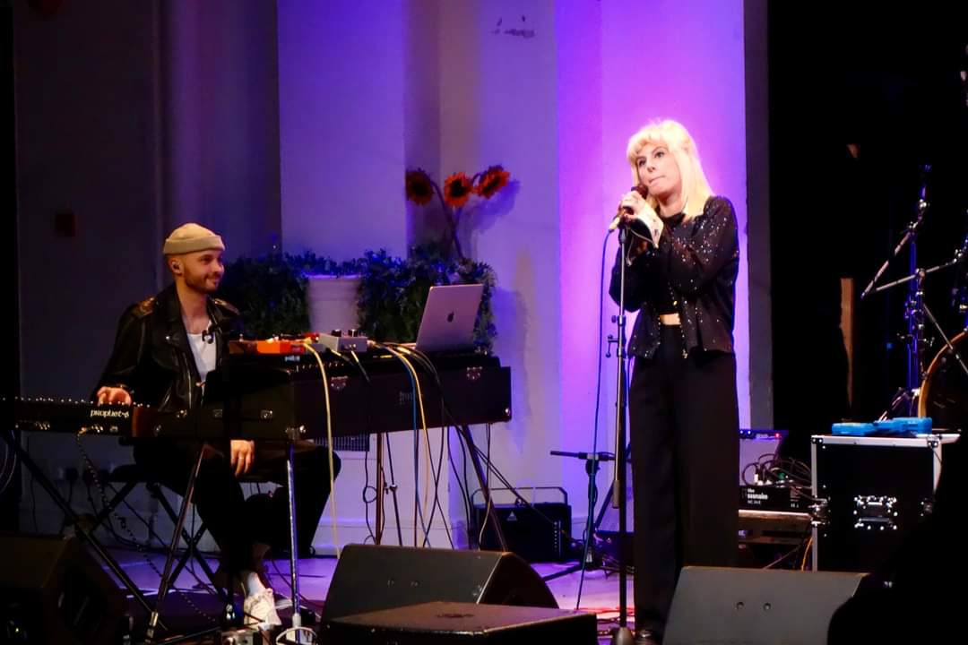 Papaya Noon onstage, featuring a keyboardist with multiple synthesizers and keyboards, and a vocalist.