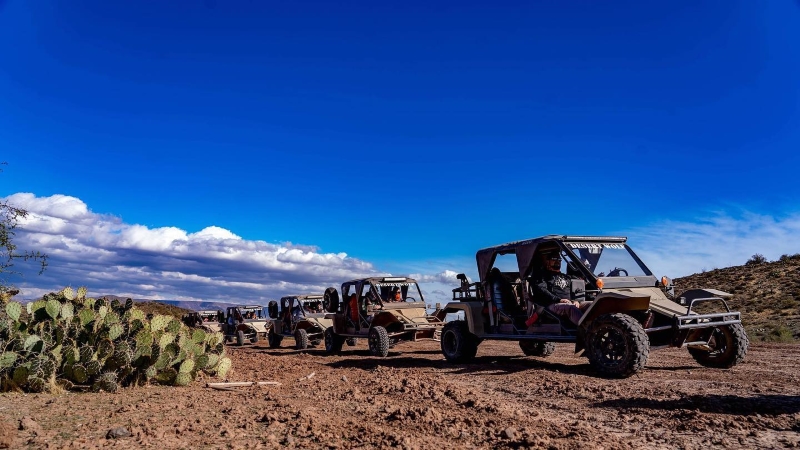 Several off-road vehicles on an excursion with Desert Wolf Tours in Phoenix. The dirt road is lined with cacti and the sky is a deep blue.