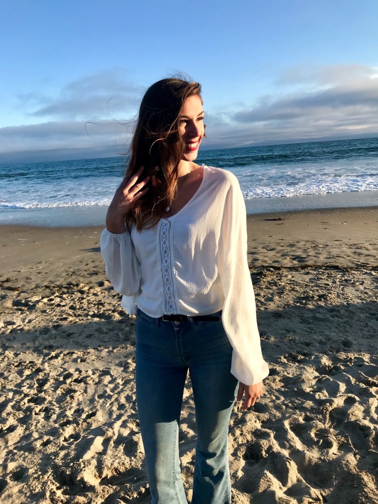 Jenna standing on Santa Cruz beach in flowing white shirt smiling toward the sun