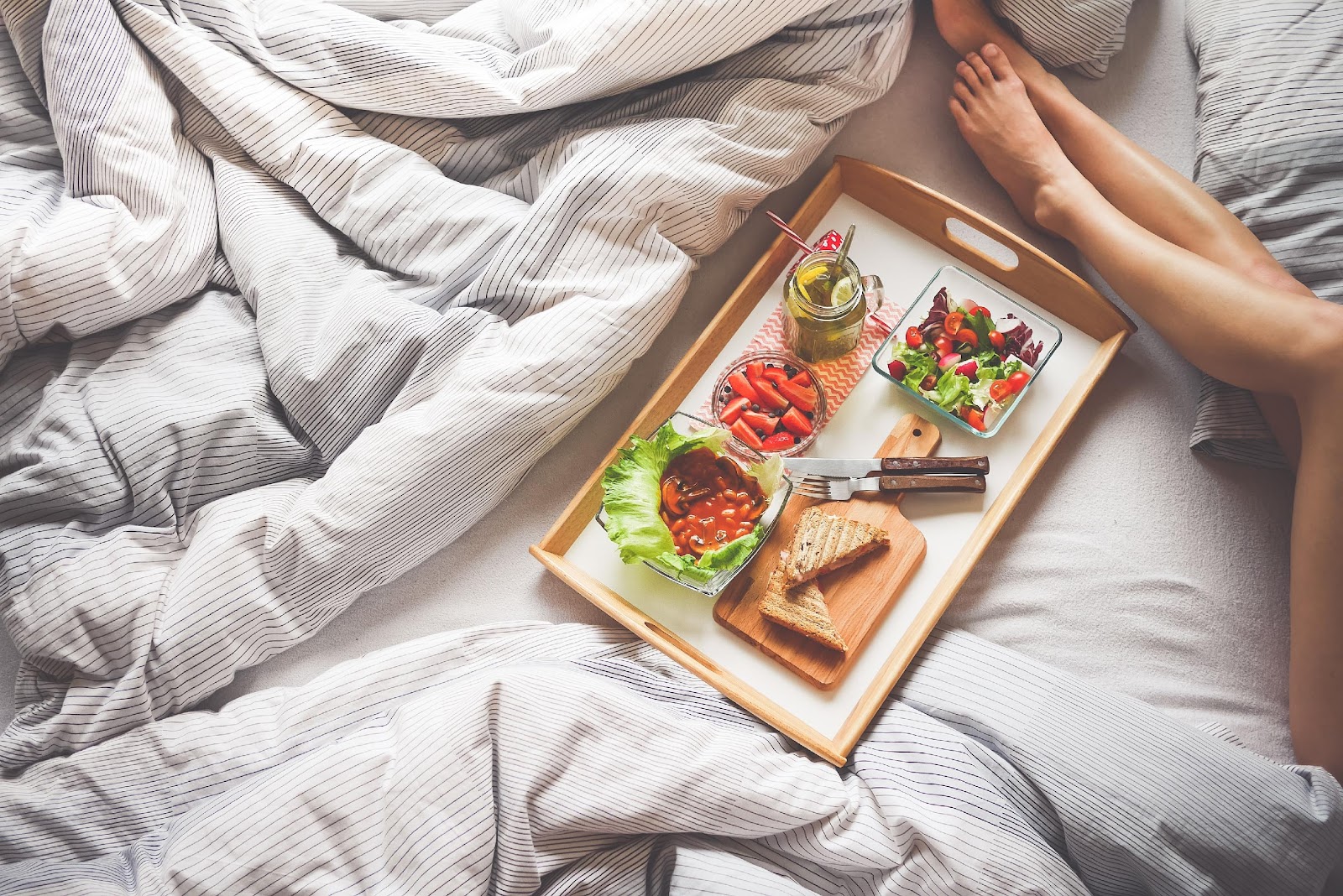 A TRAY OF FOOD ON A BED WITH A WOMEN PAIR OF LEGS 
rest is important for varicose veins