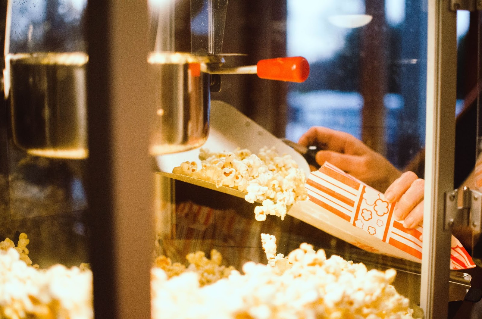 closeup of hands scooping popcorn out of a movie theatre popcorn maker