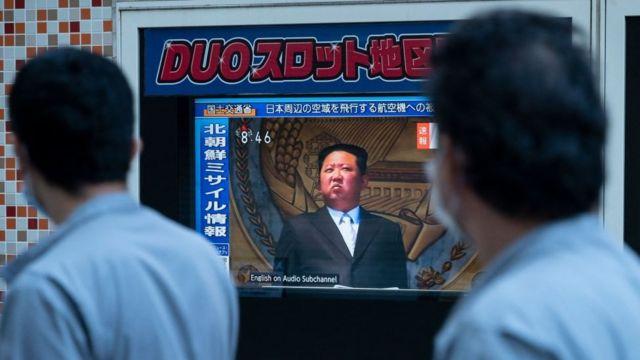 People in Tokyo walk past a TV screen showing Kim Jong-un
