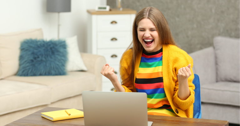 Mujer joven feliz jugando al bingo online usando un ordenador portátil en casa