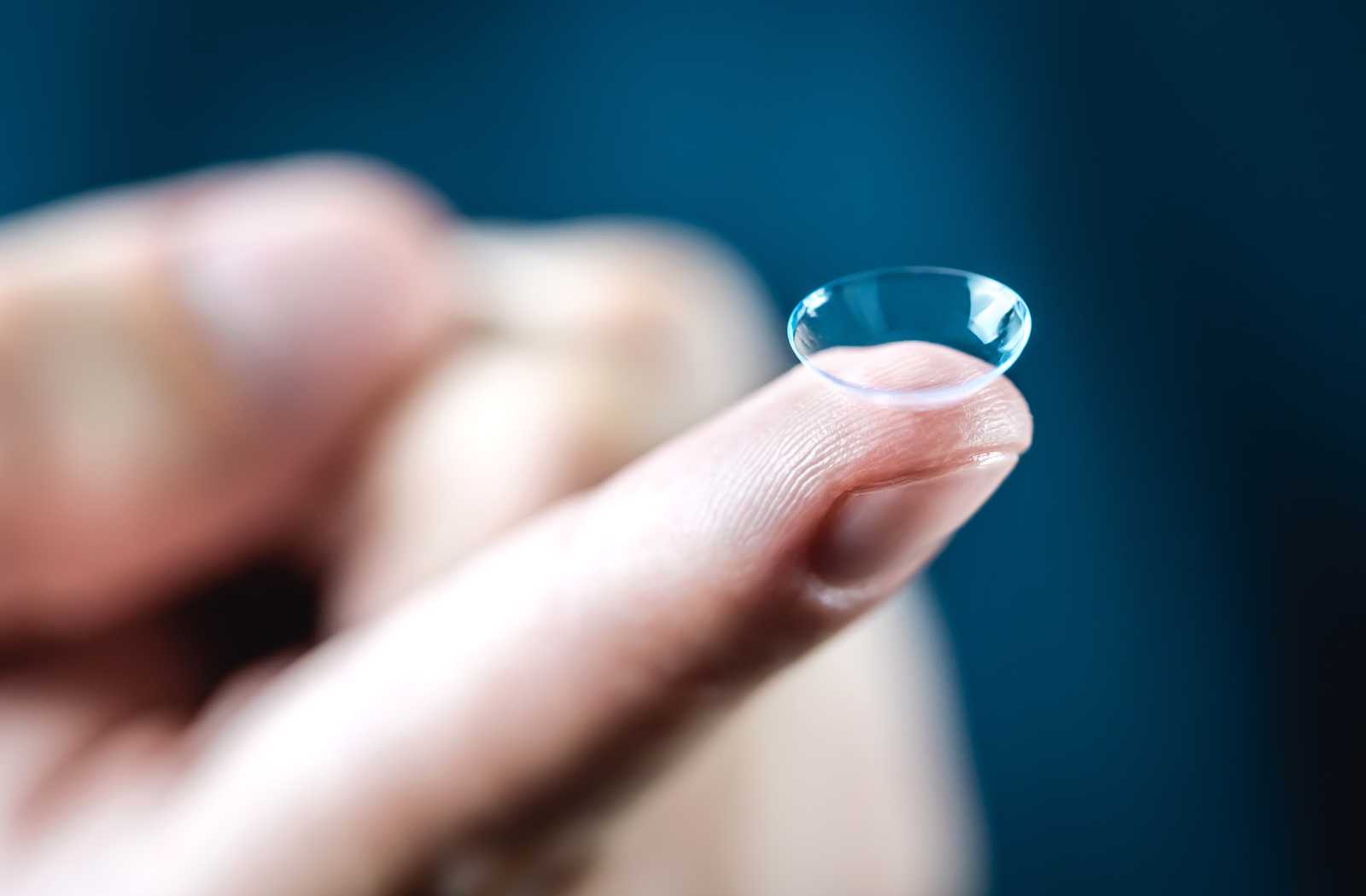 closeup of a finger holding up contact lens on dark blue background