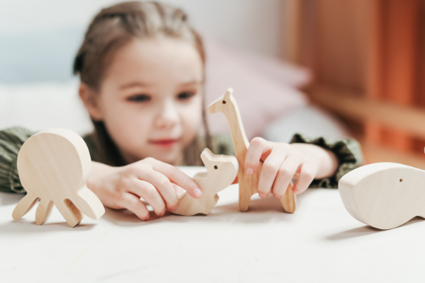 A young girl playing with wooden toy animals on a table.