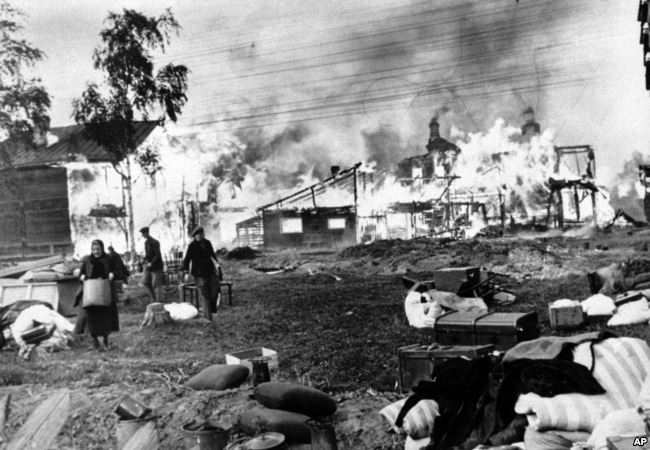 Мужчины и женщины спасают свои пожитки из горящих домов, подожжённых советскими солдатами в рамках политики выжженной земли, пригород Ленинграда, 21 октября 1941 года
