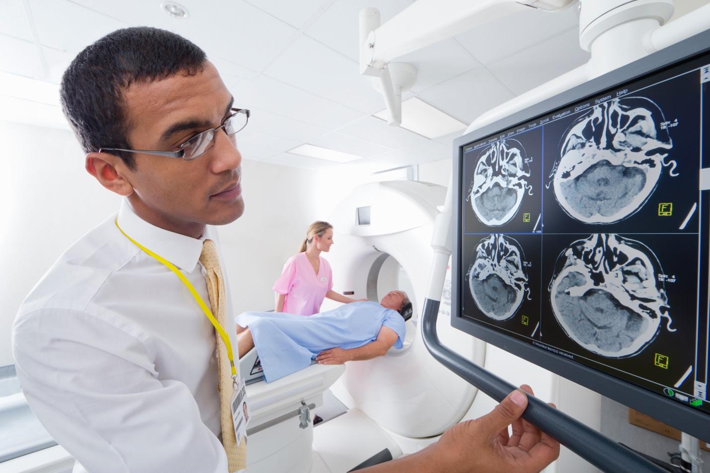 Surgeon examining digital brain scan on monitor with patient in the background