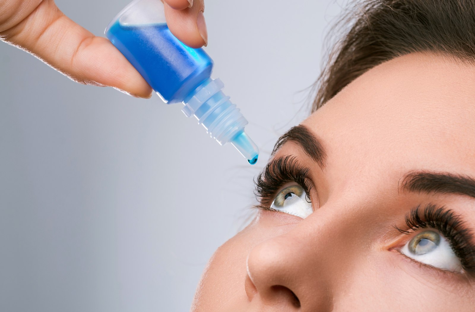 Administering blue eye drops to a lady with green eyes to relieve her symptoms of dry eye