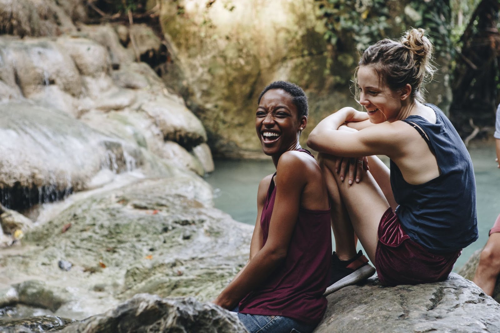 Two girls sitting on rocks beside a river and laughing.