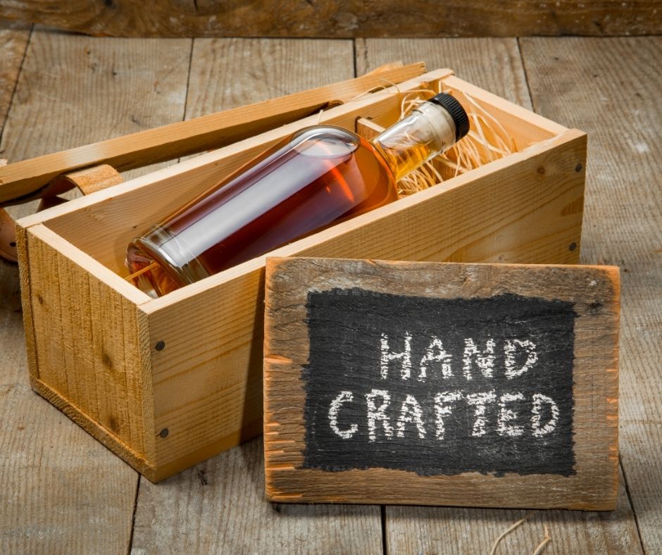 picture of a bourbon bottle in a wooden box with a sign that says  hand-crafted the bourbon gift guide