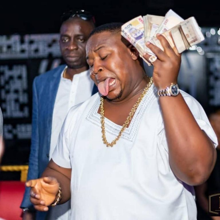 obi cubana holding bundles of naira notes to his ear with his tongue out