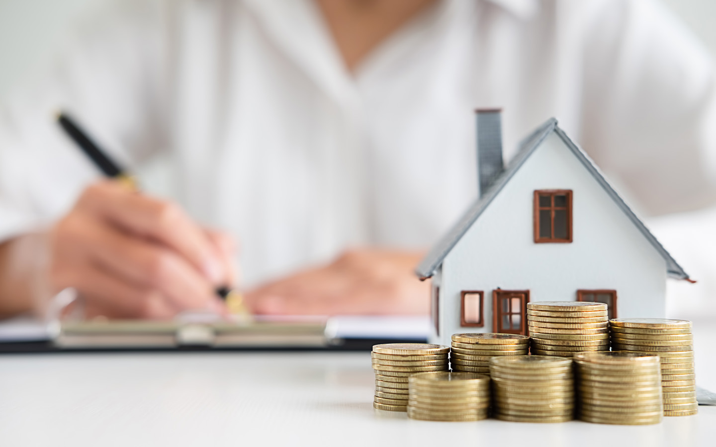 woman signing house buying contract with house model and coins on table