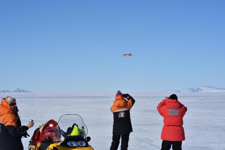 people watch a plane fly over the ice field 