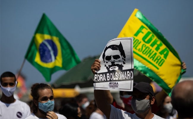 Imagem de um protesto, há uma bandeira do Brasil, uma bandeira que diz "Fora Bolsonaro" e um papel que diz "Fora Bolsonaro"