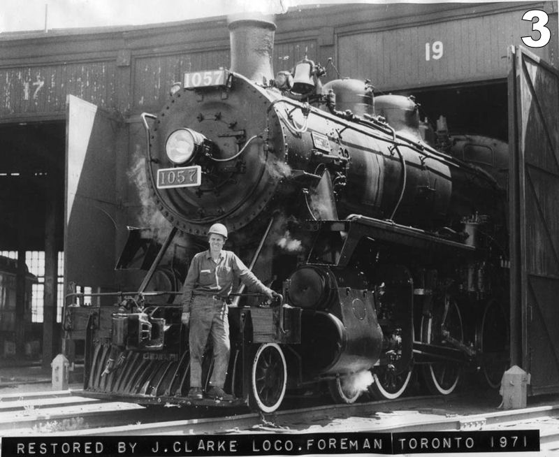 John Clarke poses in front of steam locomotive No. 10057. He is wearing work clothes and a hard hat.